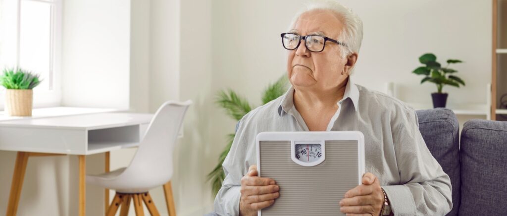 Senior man looking anxious holding a weighing scale