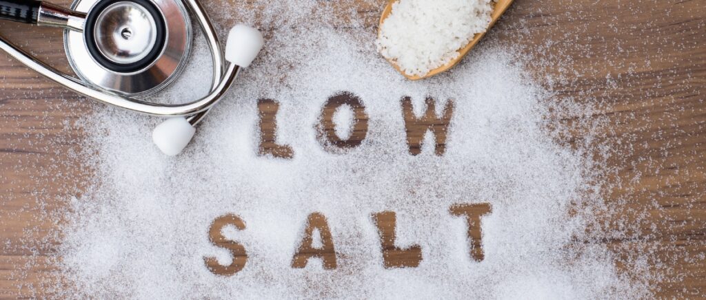 Low salt letters written in salt grains and medical stethoscope on wood table background.