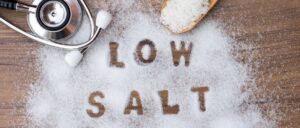 Low salt letters written in salt grains and medical stethoscope on wood table background.