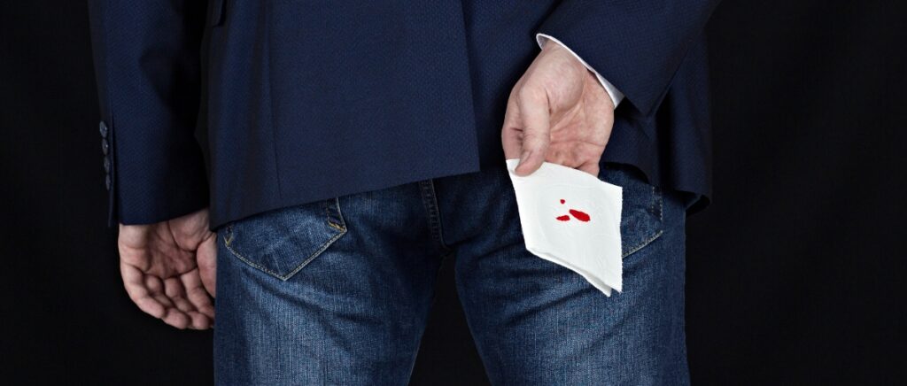 Man in suit holds toilet paper with blood