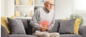 Elderly man with abdominal cramps sitting on sofa