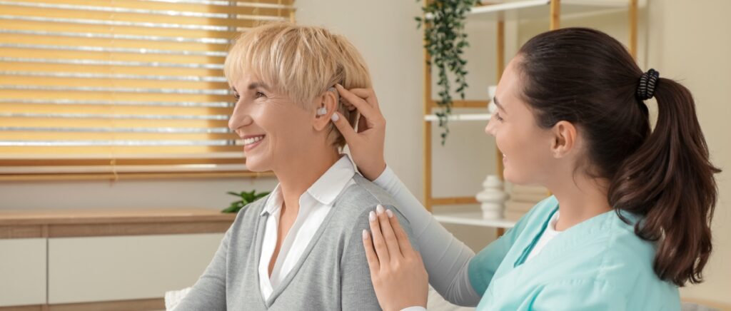Woman wondering how long do hearing aids last as doctor place a new one in her ear