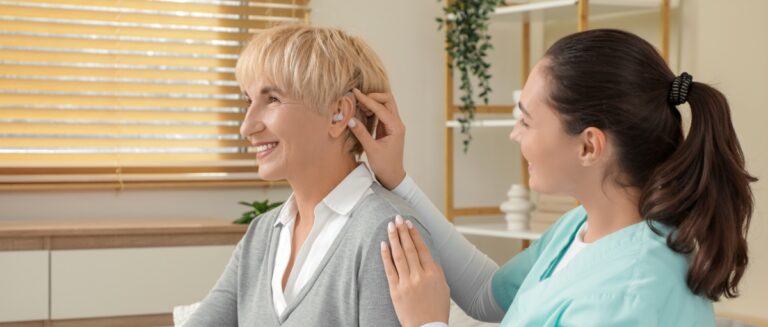 Woman wondering how long do hearing aids last as doctor place a new one in her ear